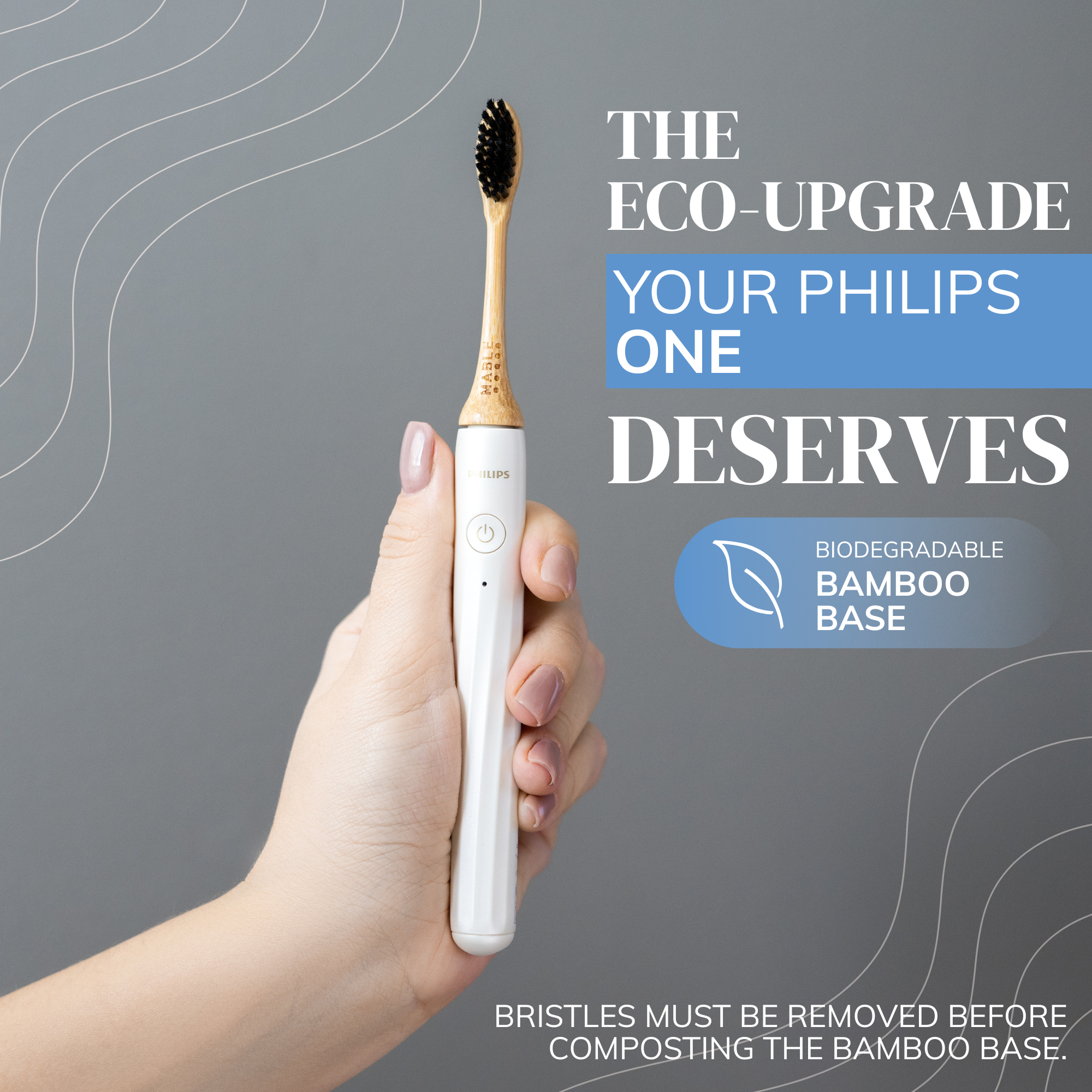 Hand holding a white Phillips one electric toothbrush with a MABLE eco-friendly bamboo electric head and text about an eco-upgrade and biodegradable bamboo base on a gray background.