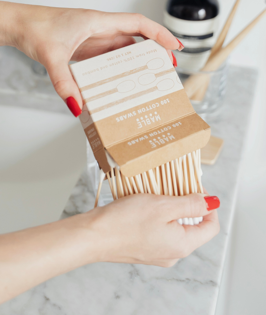 MABLE bamboo cotton swabs being held by a person tipping them out with a neutral marble background
