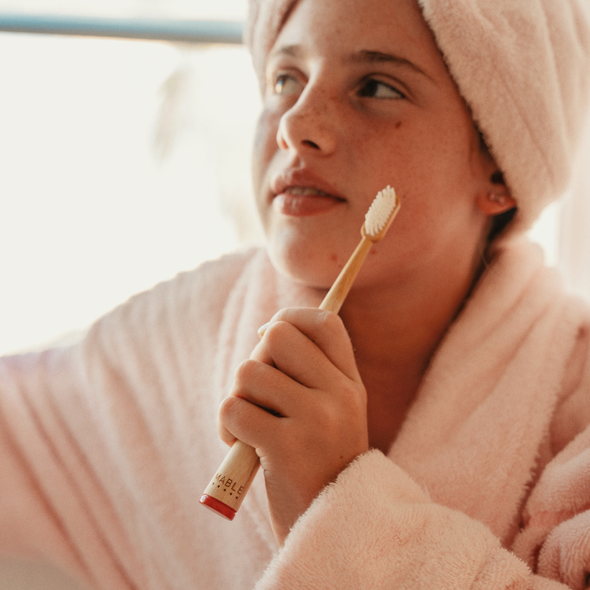 MABLE Bamboo toothbrush held by a girl in a light pink robe with soft lighting