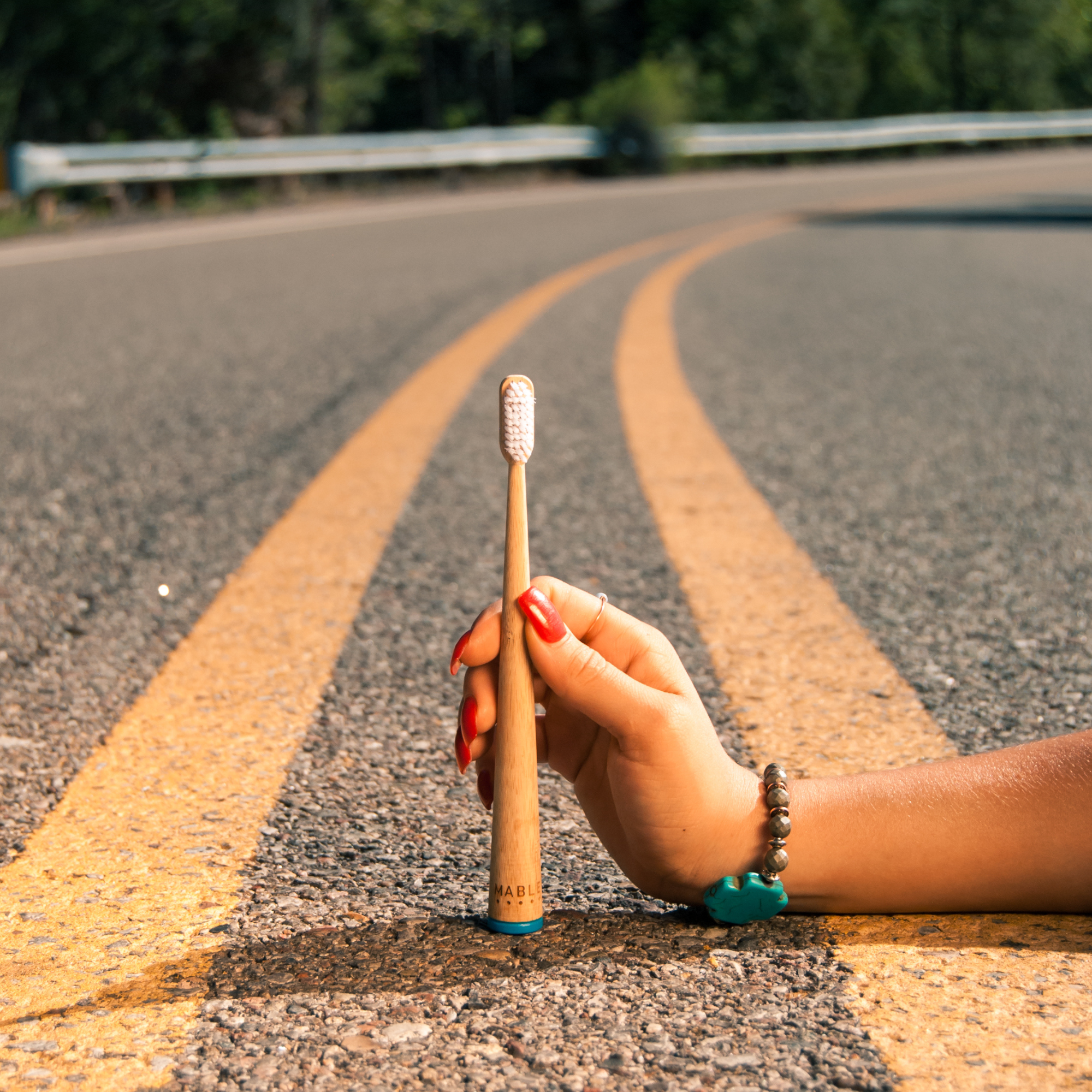Hand holding a MABLE bamboo toothbrush on a road with yellow lines envolking travel and adventure