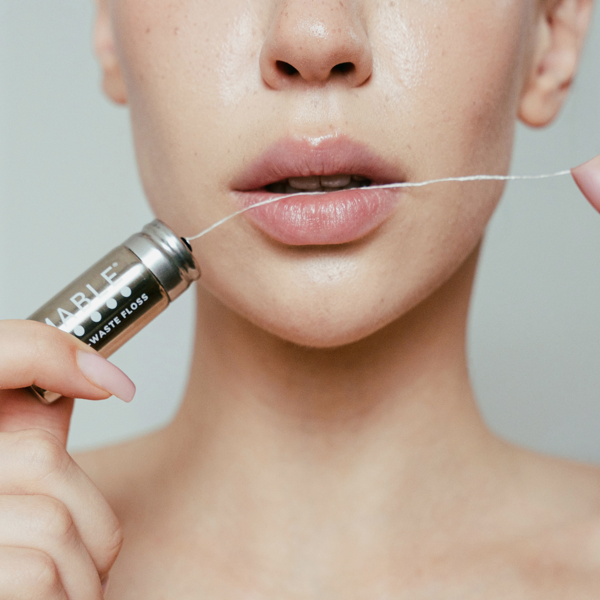 MABLE silk dental floss in a refillable floss container held by a women with plastic-free floss gliding between her teeth on a neutral background