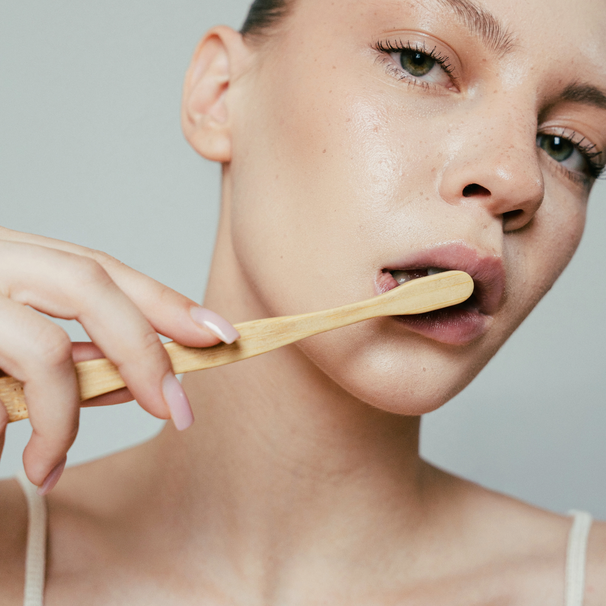 MABLE the best manual bamboo toothbrushes woman holding wooden brush with dewy skin and neutral background