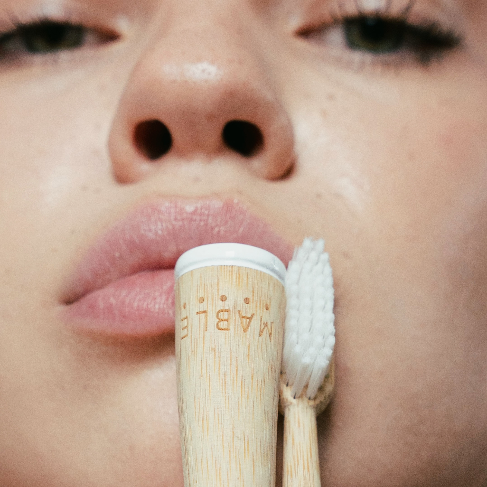 Close-up of a person holding a MABLE bamboo toothbrush with a white bristle head.