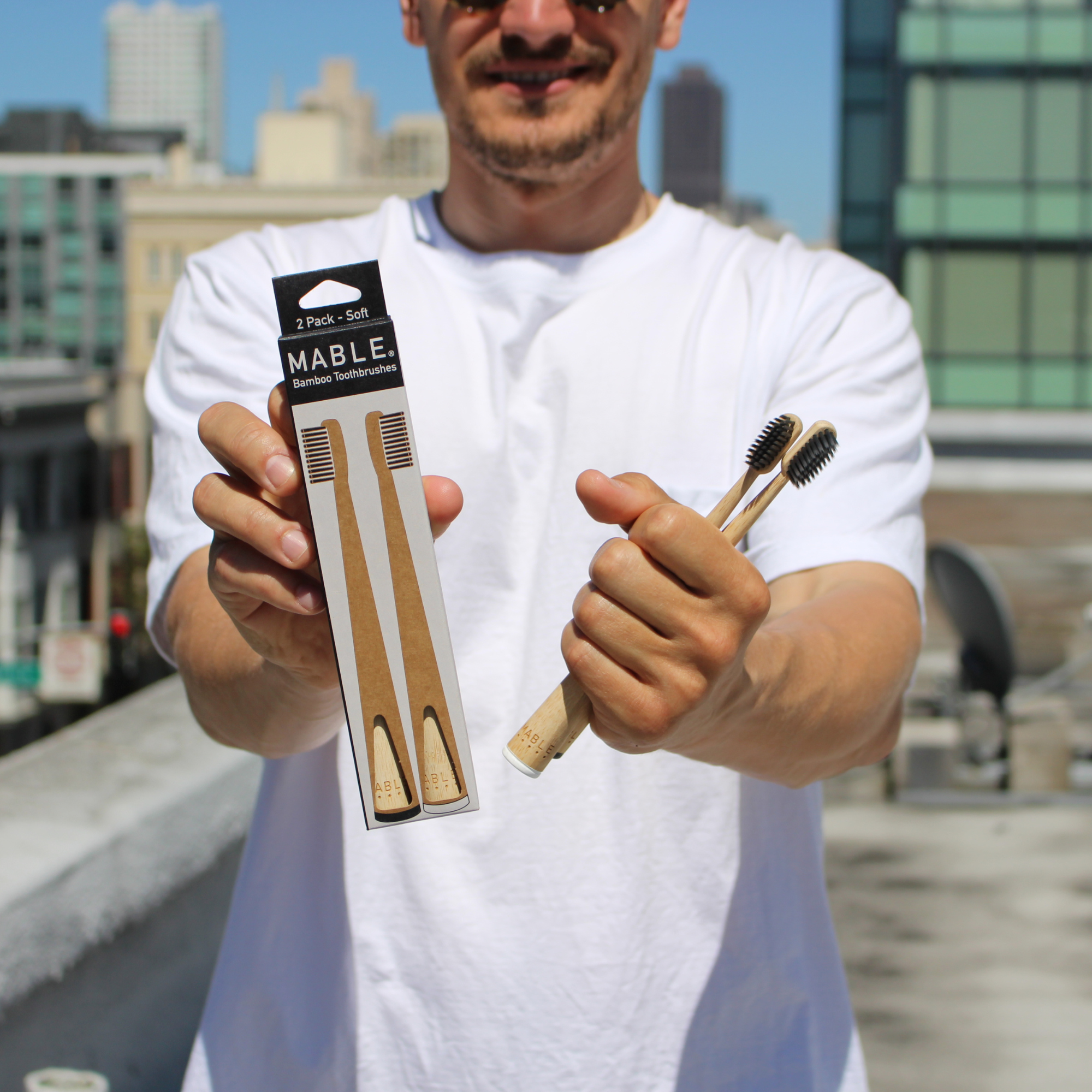 Man holding a package of MABLE bamboo toothbrushes with a cityscape in the background