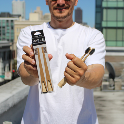 Man holding a package of MABLE bamboo toothbrushes with a cityscape in the background