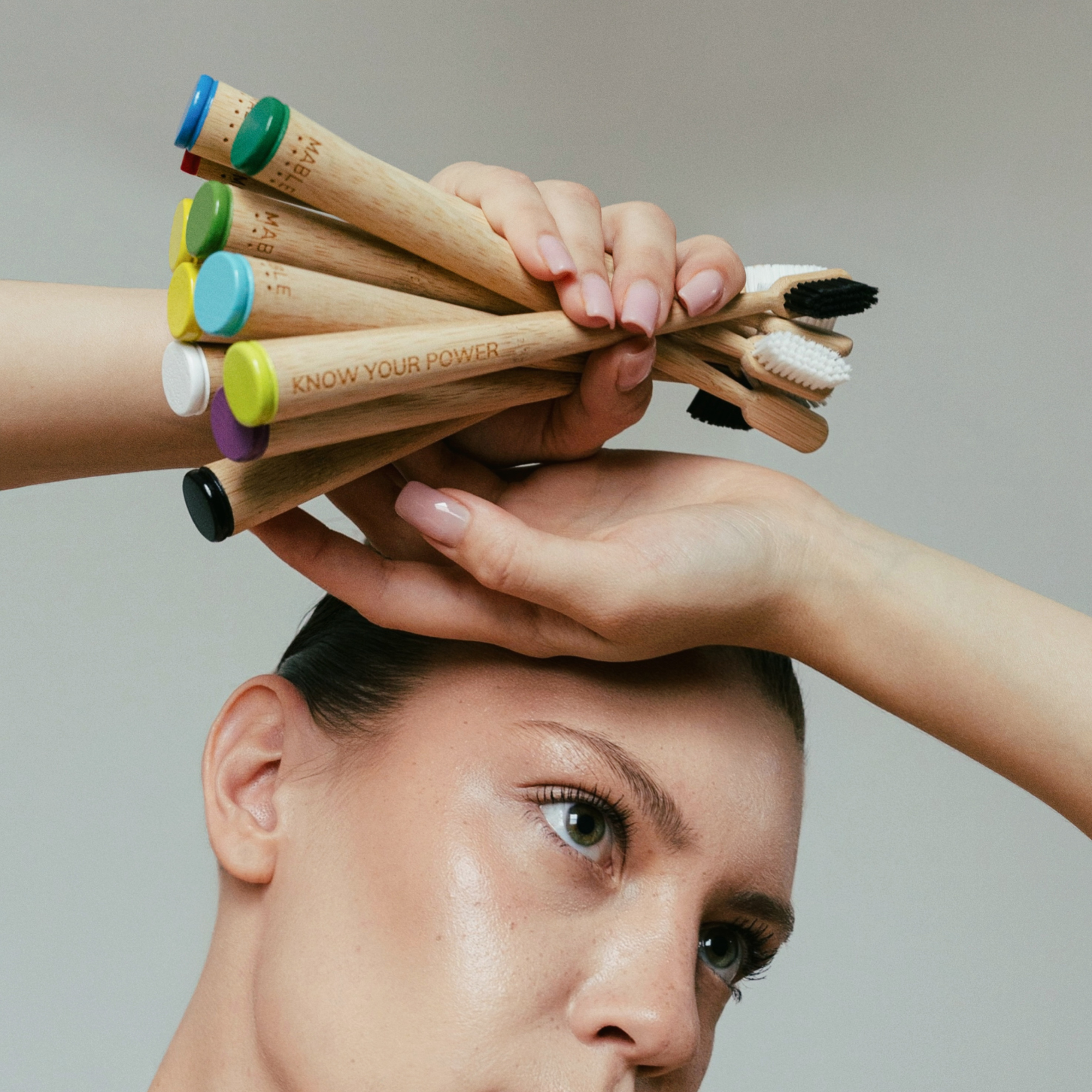 Person holding a bundle of MABLE bamboo toothbrushes above their head with a neutral background