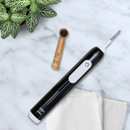 MABLE bamboo toothbrush head for Oral-B on top of a marble countertop with white towel and green plant in the backdrop