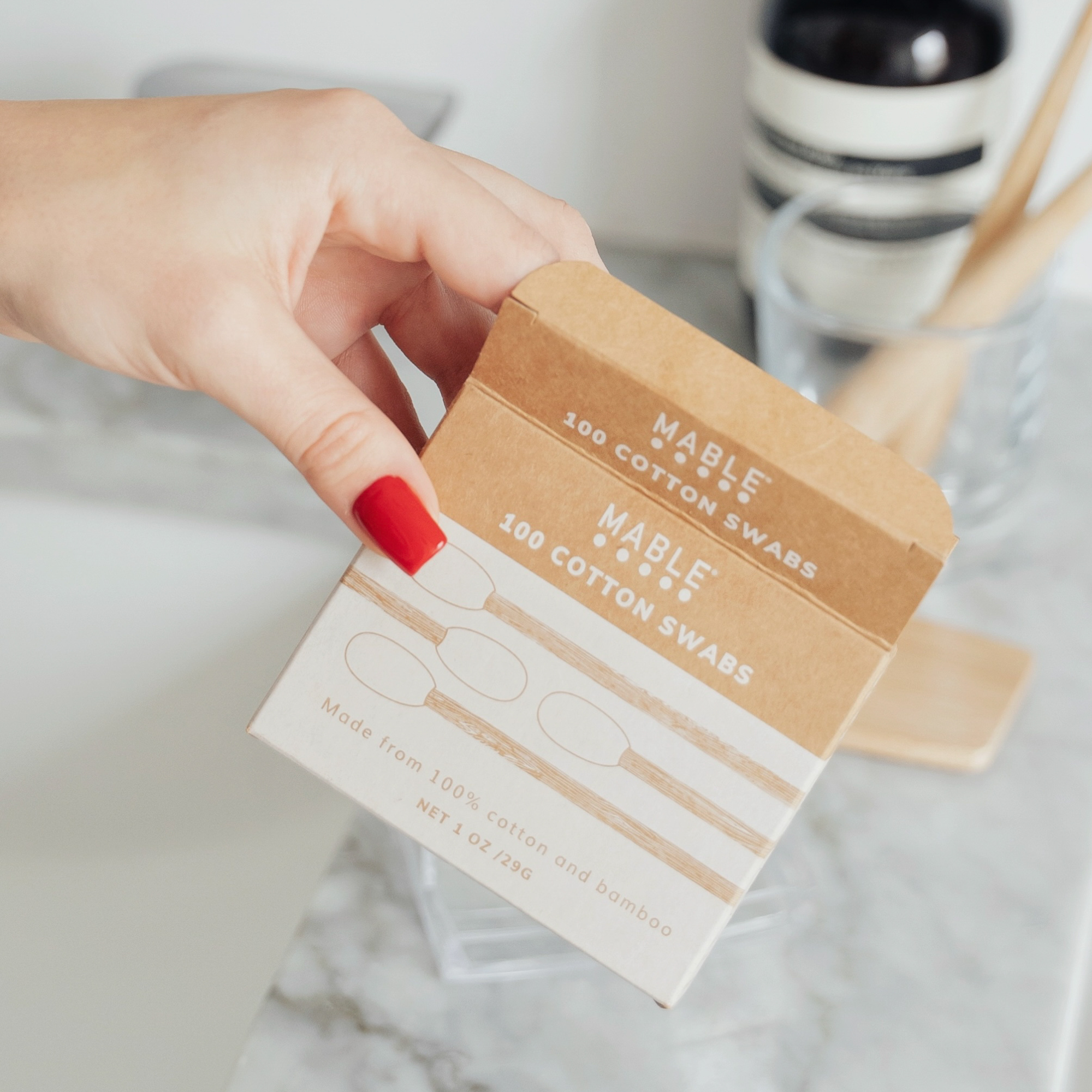 Hand holding a box of Mable Cotton Swabs on a marble surface.