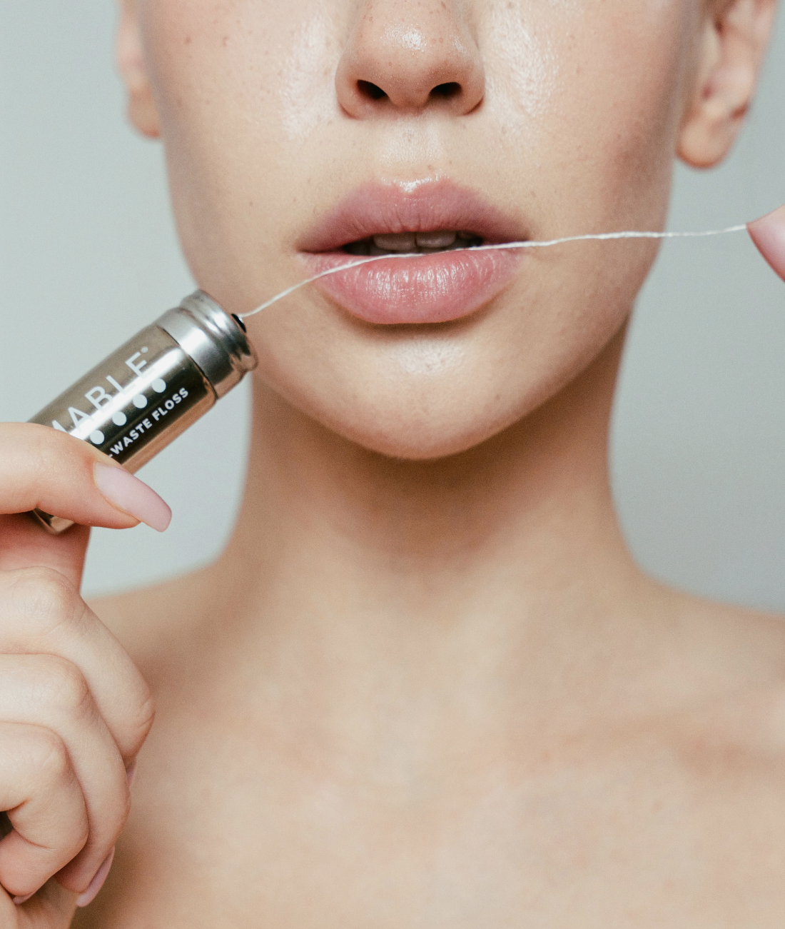 The best compostable dental floss by MABLE, woman holding stainless steel refillable floss container and flossing with MABLE biodegradable floss