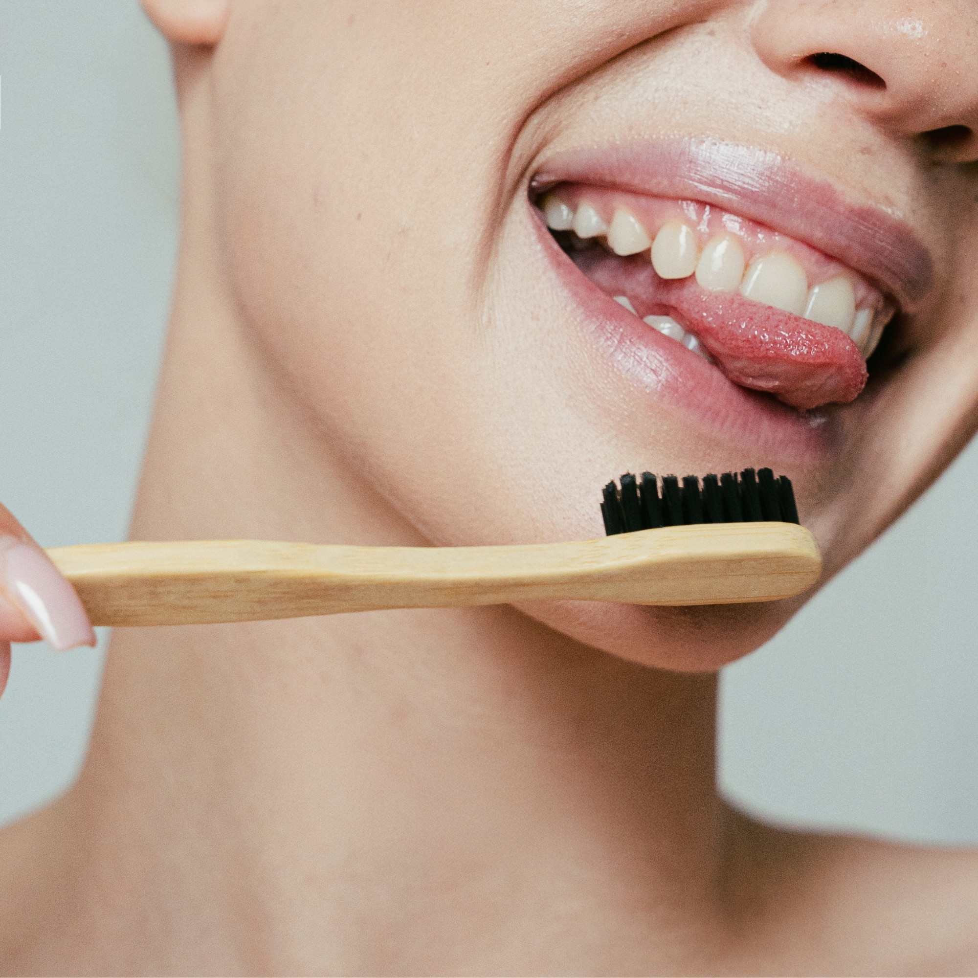 The best eco toothbrush by MABLE, a person holding a bamboo toothbrush with black bristles near their smiling mouth