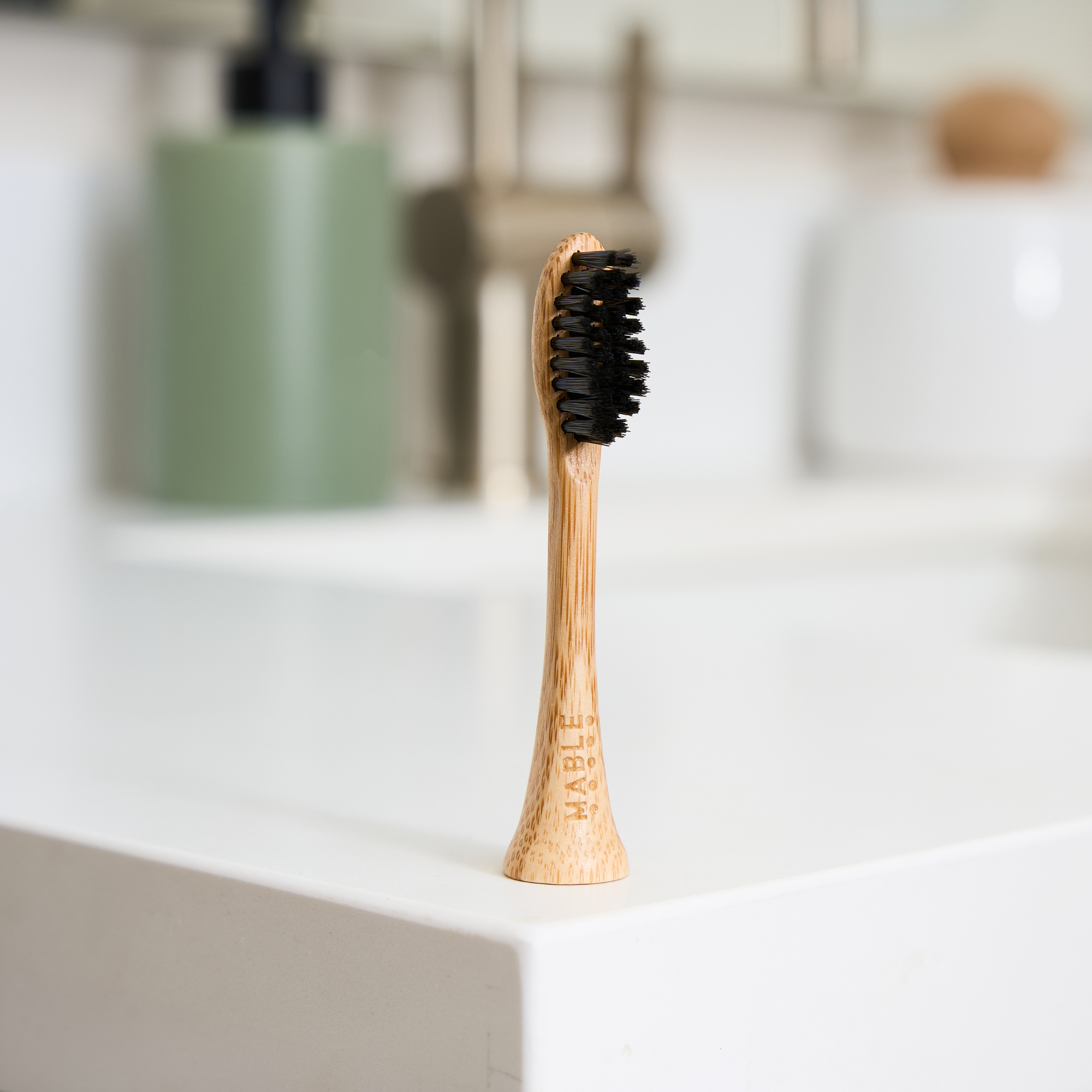 MABLE electric bamboo toothbrush head with soft plant-based bristles standing upright on a white countertop, with a blurred bathroom background.