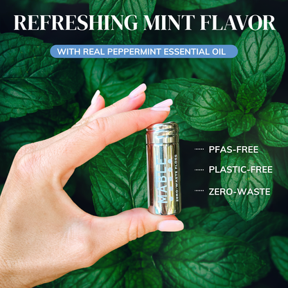 Hand holding MABLE refillable floss container with mint leaves in the background, emphasizing a refreshing mint flavor and zero-waste product.