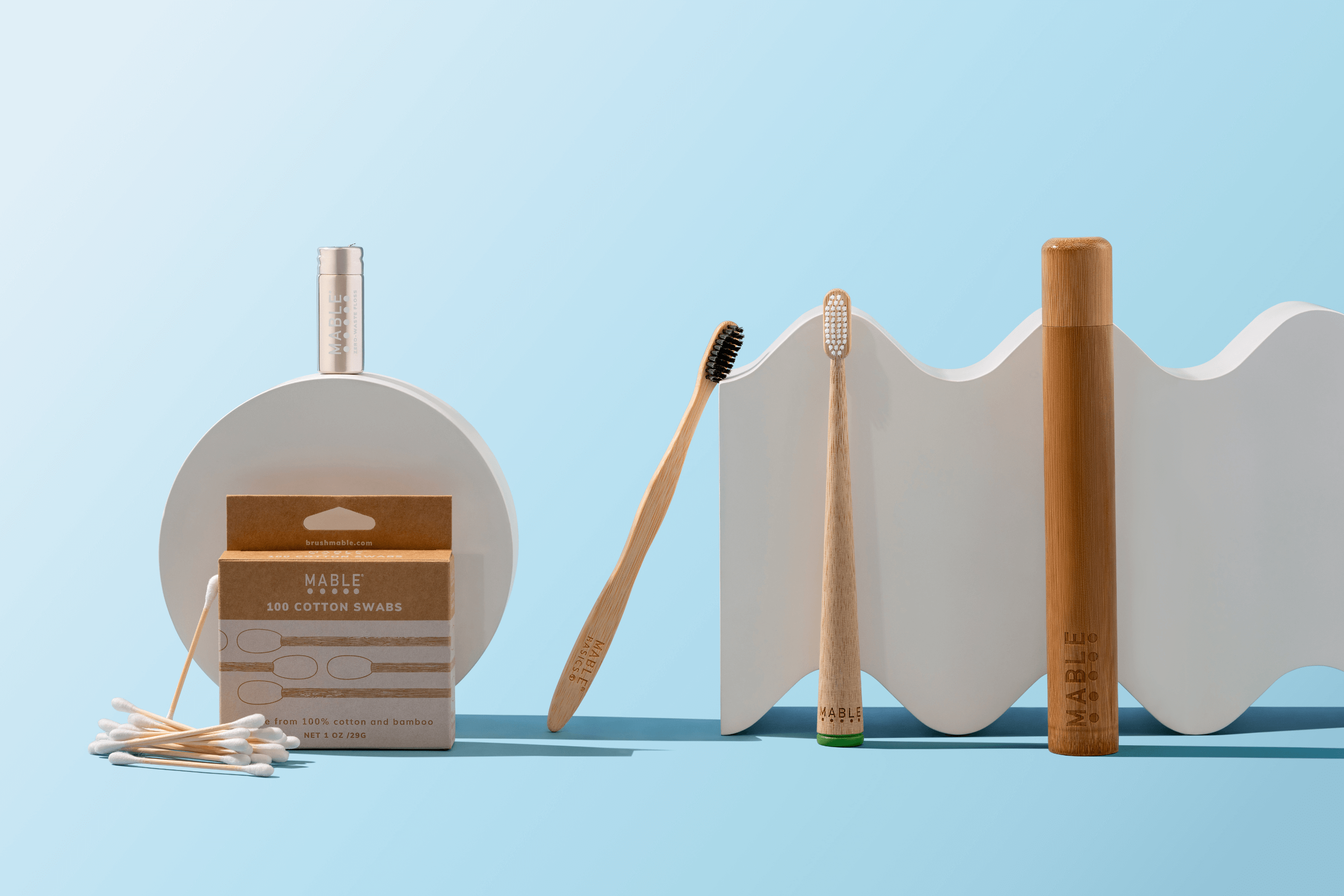 MABLE Eco Friendly Bathroom Supplies including bamboo toothbrushes, compostable dental floss, bamboo cotton swabs, bamboo travel case on a light blue background