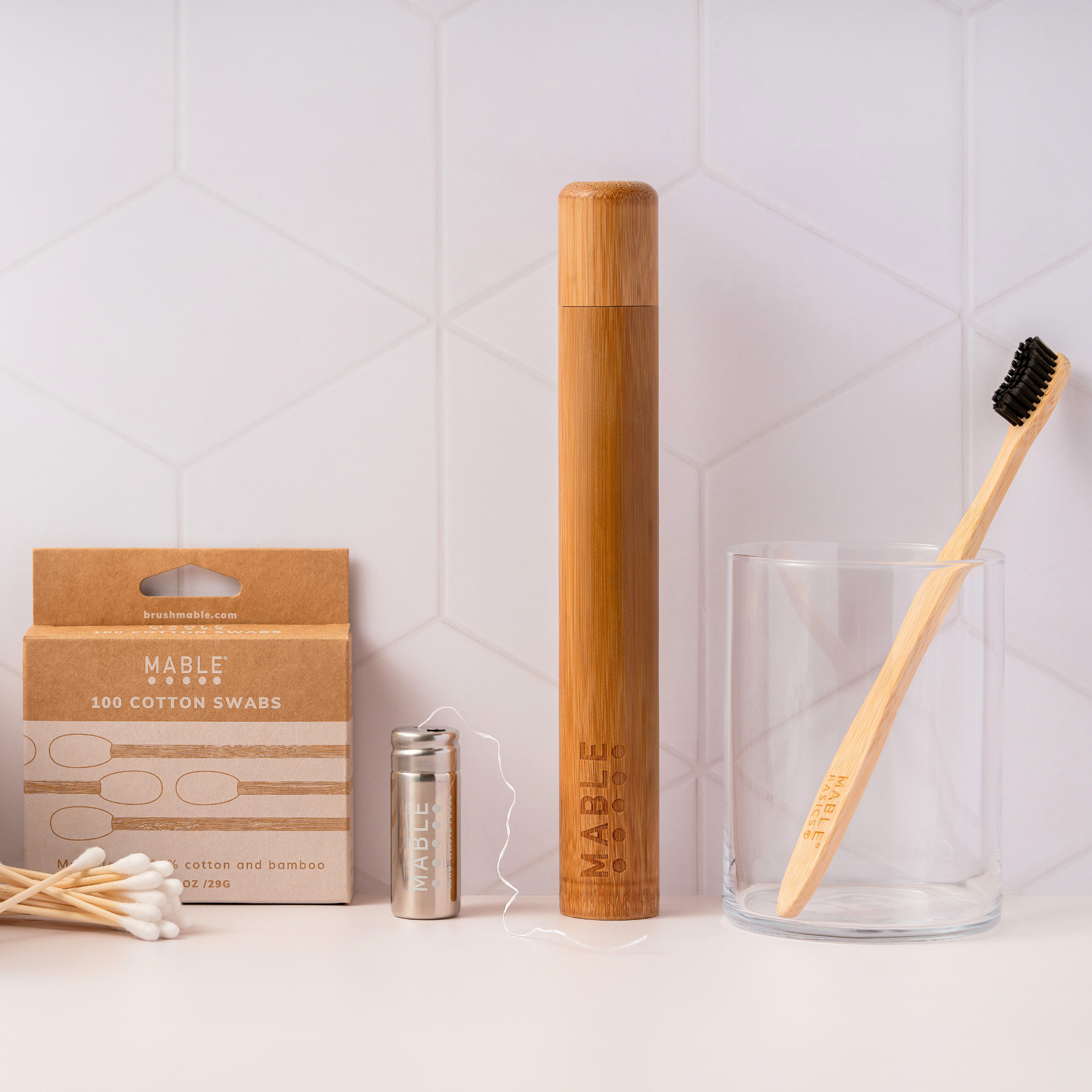A selection of sustainable travel essentials including a MABLE travel case, bamboo toothbrush, refillable floss and bamboo cotton swabs