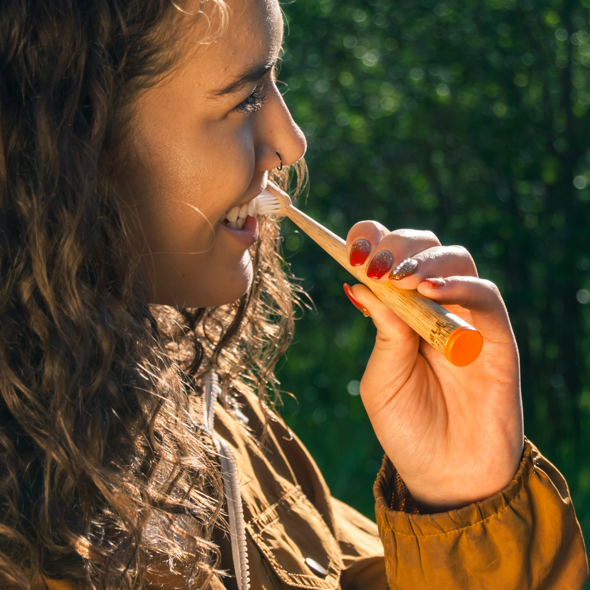 Woman brushing her teeth outdoors with a MABLE bamboo toothbrush blurred green background
